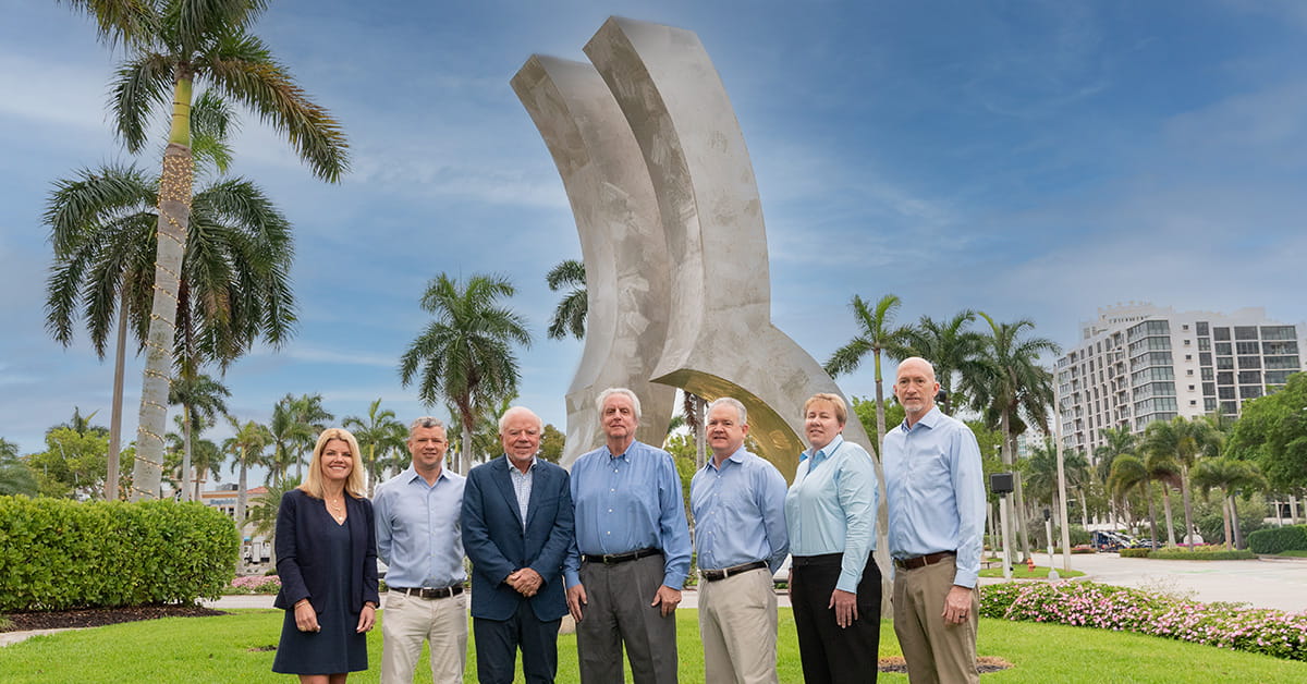 Executive leadership team standing outdoors near sculpture and palm trees