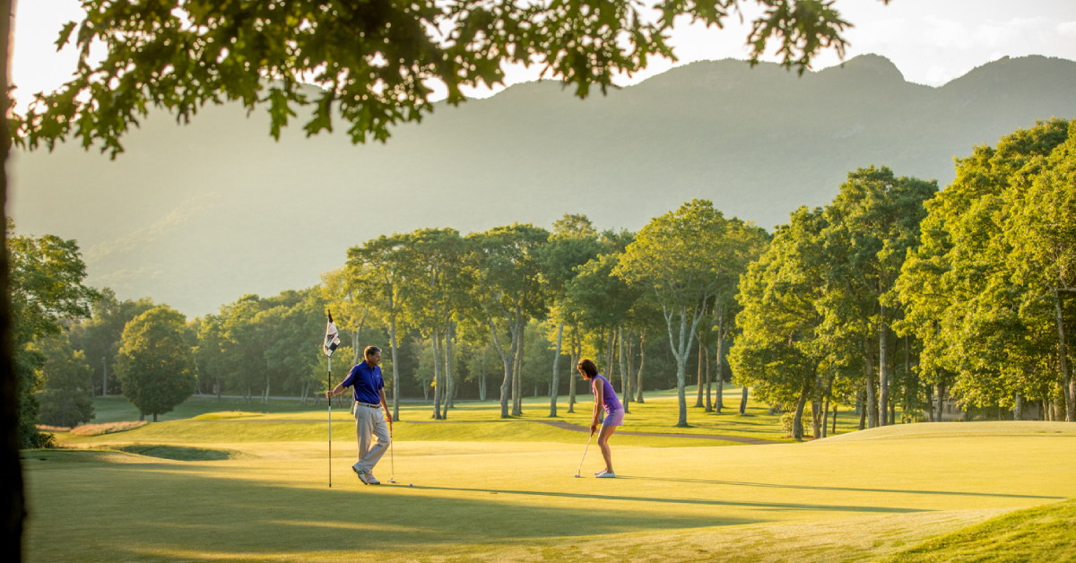 Two golfers on a sunlit putting green at Linville Ridge, with trees and mountains
